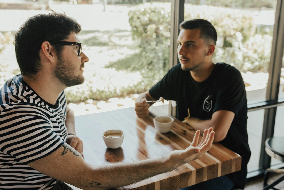 Two men in an honest conversation across a table, leaning in