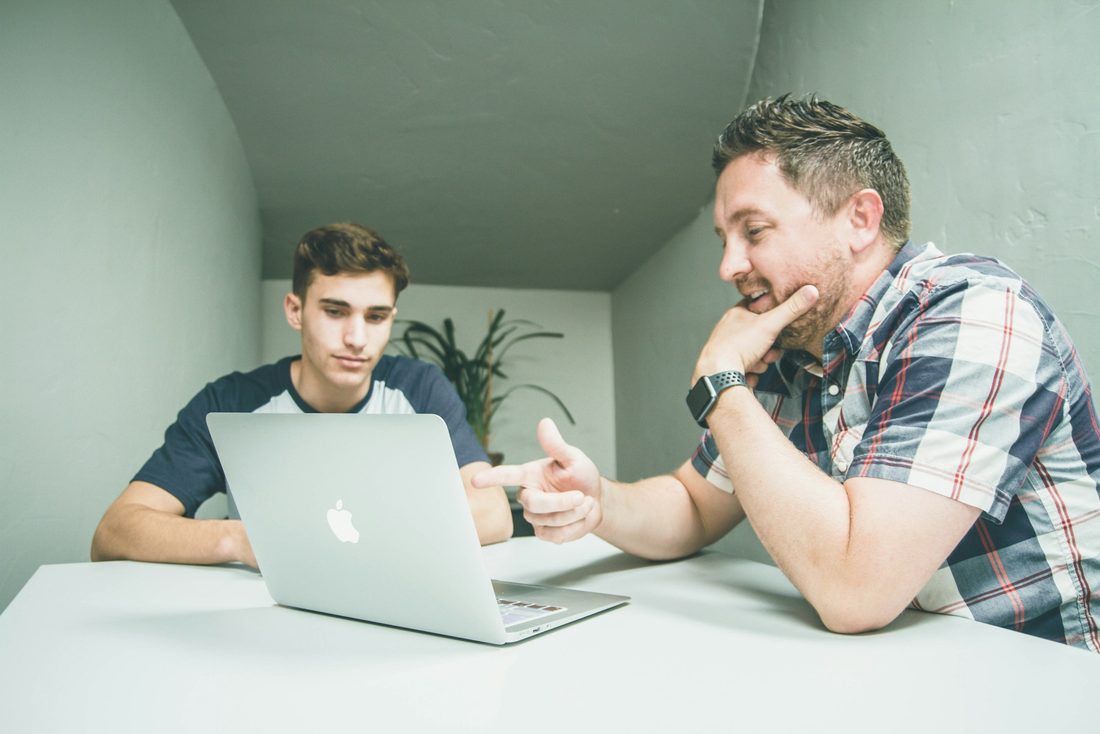 An older mentor guiding a younger man, pointing something out as they work together