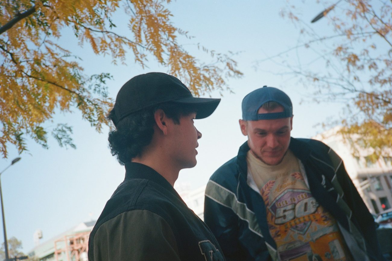A young man listening closely as an older man talks with him outdoors in warm autumn light
